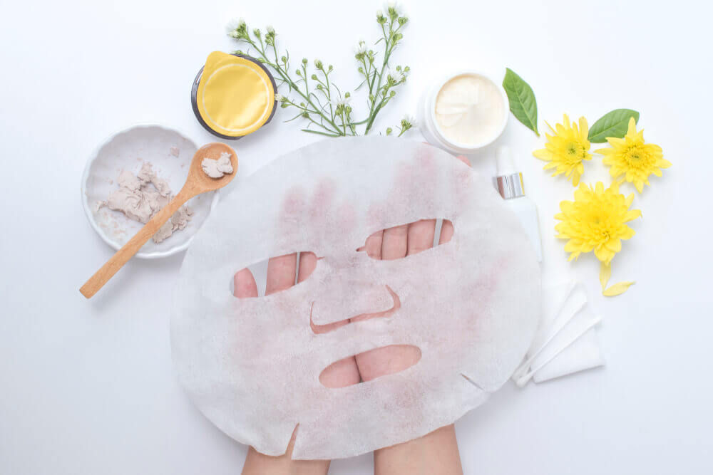 Hands holding a sheet mask surrounded by natural ingrediants