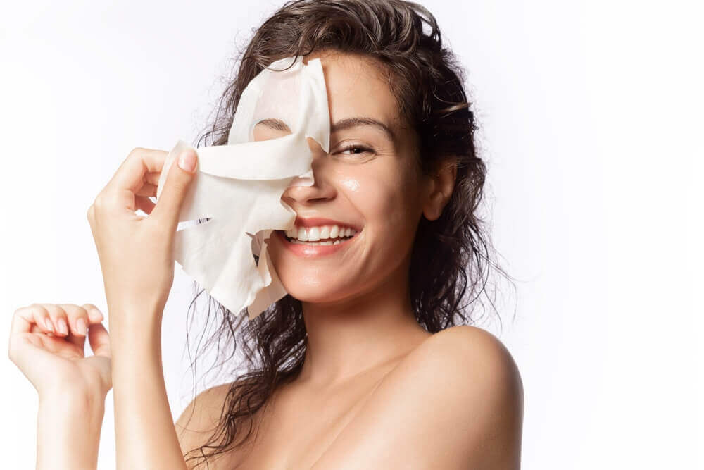 woman peeling off a sheet mask and smiling